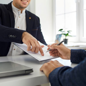 Two men sit at a table with a laptop and paper to be filled, and an Estate Planning Attorney and Trust Administrator are discussing. - Law Office Of Kent P. Woods